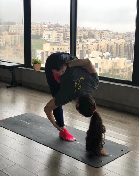 Diala in a standing forward fold by a window overlooking Amman